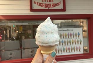 Stacy's hand holding an ice cream cone convered with a white dip with flecks of confetti