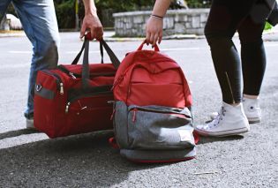 Lower bodies of people holding a duffel bag and backpack
