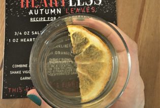 Top down view of a hand holding a light orange cocktail garnished with a dried grapefruit slice