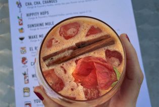 Stacy's hand holding a pink cocktail garnished with a cinnamon stick and flower