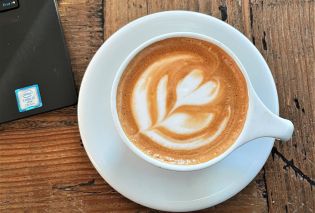 Top down view of a cappucino with foam art and the edge of a laptop keyboard