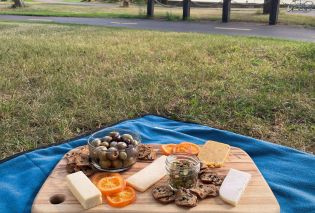 Cheese board on a picnic blanket with a path and lake in the background