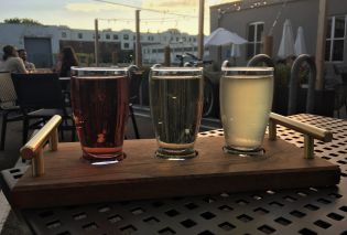 Flight of three small glasses of cider on a wooden tray 