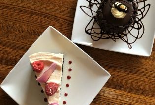 Top down view of piece of cheesecake garnished with raspberries and an individual chocolate cake