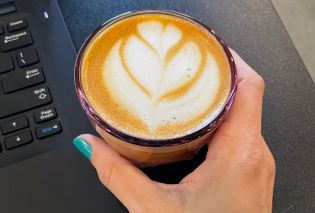 Hand holding a cappuccino in a small pink glass with foam art