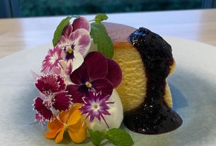 Piece of cheesecake garnished with fresh flowers and blueberry jam