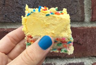 Side view of a hand holding a funfetti cookie bar with a thick layer of yellow frosting