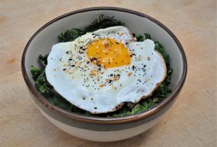 Bowl filled with sauteed kale and topped with a fried egg and everything bagel seasoning