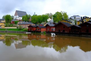 Red wooden buildings along a river with colorful wooden houses and a church in the background