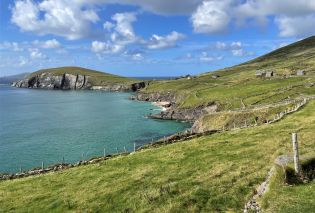 Green grassy hills surrounding an ocean cove with a bright blue sky