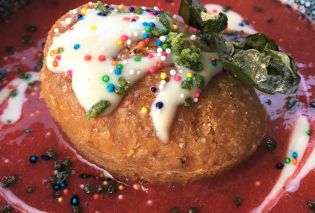 Round fried cake topped with white icing, rainbow sprinkles, and fresh mint leaves in a bowl of strawberry soup at Tongue in Cheek, St. Paul