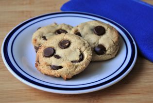 Three chocolate chip cookies on a small white plate with a blue edge