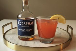 White marble tray with bottle of whiskey and cocktail garnished with a lemon slice