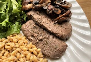 Close up of venison steak on a white plate with barley, mushrooms, and mixed greens